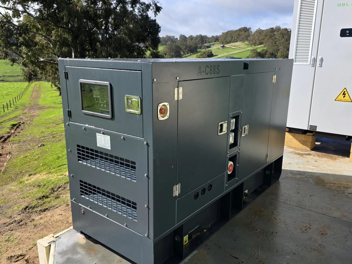 Diesel generator in a sound-proof enclosure on a concrete pad, with a control panel, emergency stop and power outlets